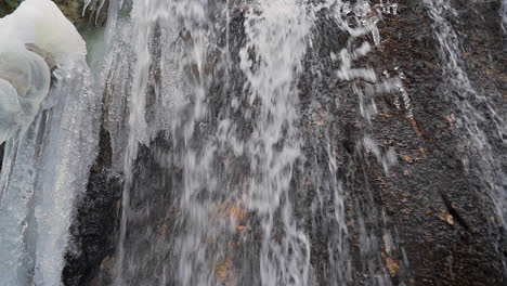 Spring-water-flowing-down-waterfall-with-icicles-in-winter,-slider-shot