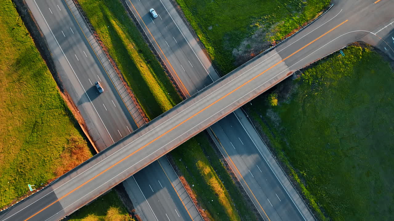 Car crosses the freeway above two highways. Green grass growing around the roads. Top view.