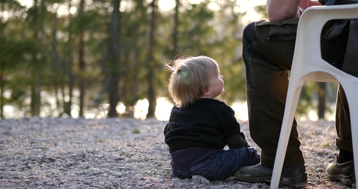 Bambino seduto accanto a un membro della famiglia all'aperto, che guarda in alto e ammira papà o nonno. Spazio per copia IDOL.