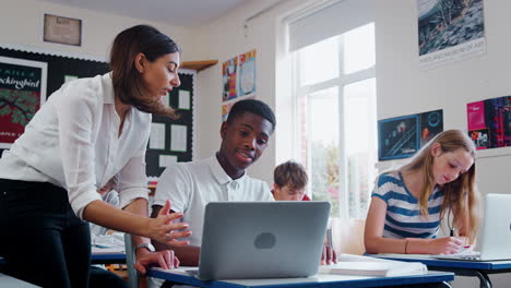 female teacher helping male pupil using computer in classroom