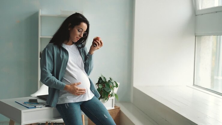 Young happy pregnant woman with healthy lifestyle. Woman eats an apple and massages her belly. Copy space.