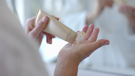 applying lotion, mature woman squeezing cream from tube onto hand in bathroom