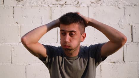 joven caucásico que se siente molesto, agarra el cabello con las manos contra la pared blanca al aire libre