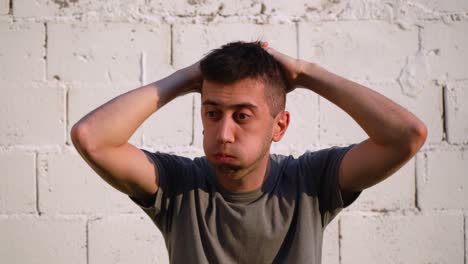 young caucasian man feeling upset, grabs hair with hands against white wall outdoor