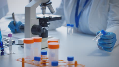primer plano de un trabajador de laboratorio que realiza investigaciones utilizando un microscopio que sostiene un tubo de ensayo etiquetado zeta