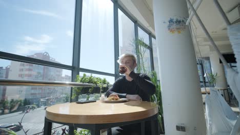 joven disfrutando de una bebida y comida en un café moderno con vistas a la ciudad