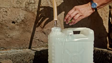 persona vertiendo agua en un tanque de plástico usando un dispensador exterior, vista estática de primer plano