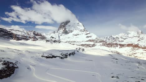 Aerial-wide-shot-of-skiers-ski-on-Zermatt-slope-near-Matterhorn-mountain-peak,-Switzerland