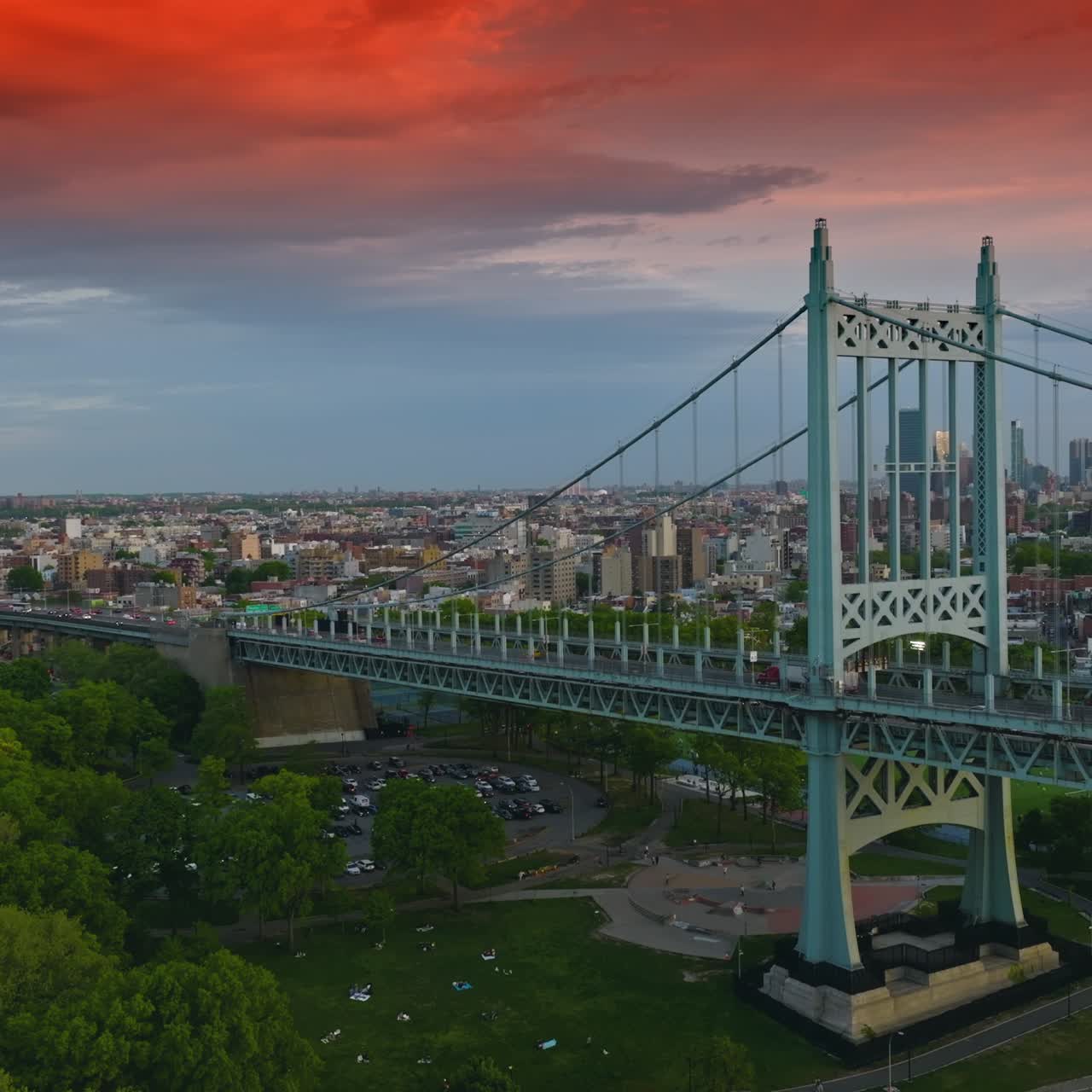Triborough Bridge under the blue and red sky at sundown. Round parking lot and sports ground under the bridge. New York scenery at backdrop