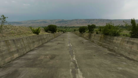 Dried-up-concrete-riverbed-with-small-rivulet-and-bushes-on-shore,-Georgia