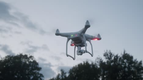 a flashing drone in front of some trees rising up into the blue cloudy sky