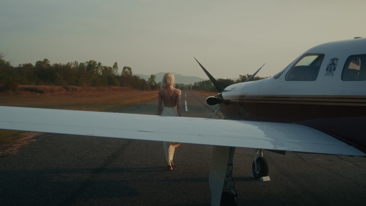 Woman walking towards a small plane at sunrise/sunset