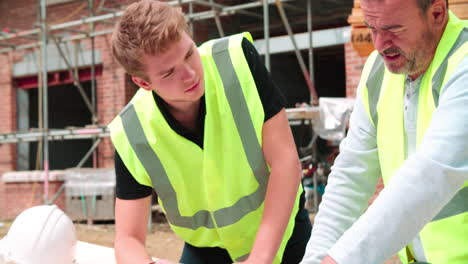 builder on building site discussing work with apprentice