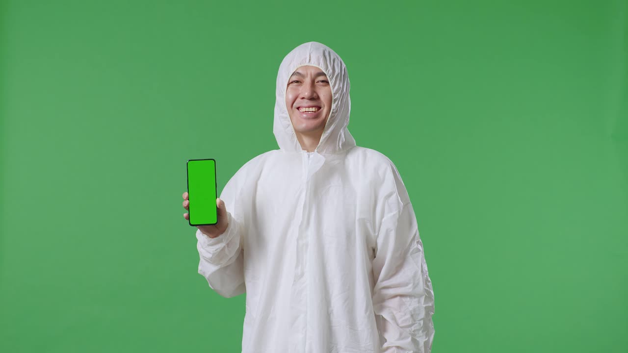 científico masculino asiático sonriendo y mostrando un teléfono inteligente de pantalla verde mientras está de pie en el fondo de la pantalla verde