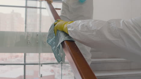 vista de cerca de las manos del hombre de limpieza con guantes limpiando las barandillas de las escaleras dentro de un edificio de oficinas