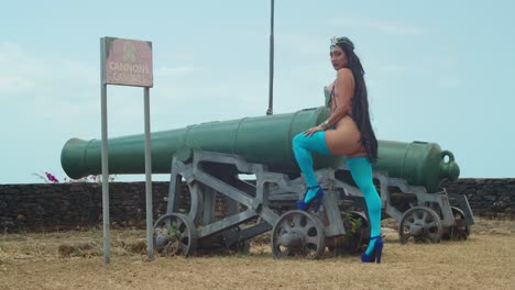 a young girl stands confidently in her eye-catching carnival costume and high heels, striking a pose beside the historic cannons at the fort in a vibrant caribbean setting