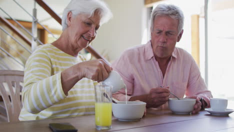 Pareja-Caucásica-Mayor-Vertiendo-Leche-En-Un-Tazón-De-Cereal-Desayunando-Juntos-En-Casa