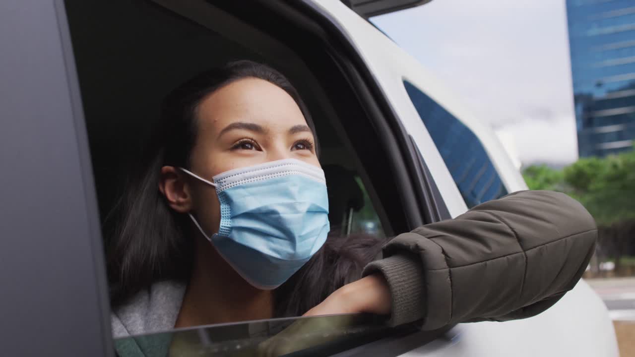 mujer asiática con máscara facial mirando por la ventana mientras está sentada en el coche