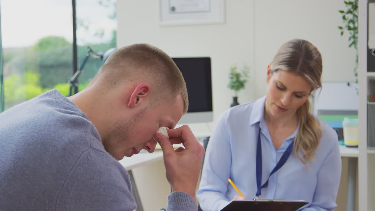 Doctor Talking To Crying Young Male Patient Suffering With Mental Health Problems