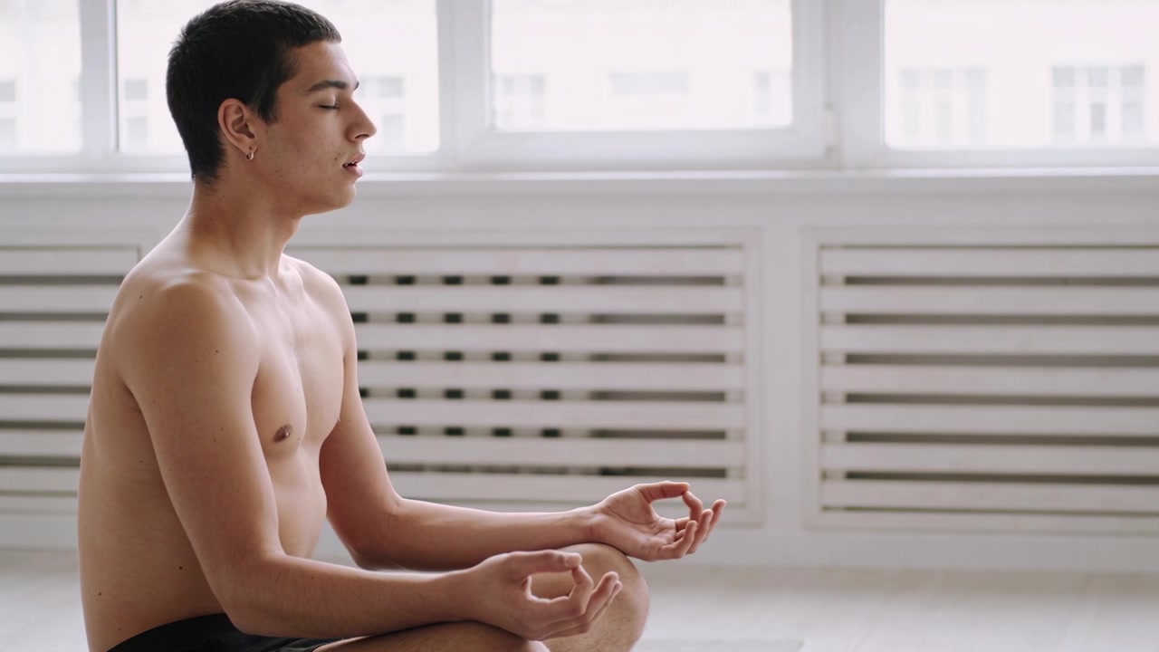 Luce solare che illumina un uomo a torso nudo in pantaloncini con orecchini a cerchio, che respira lentamente accanto alle finestre, con spazio per il testo.