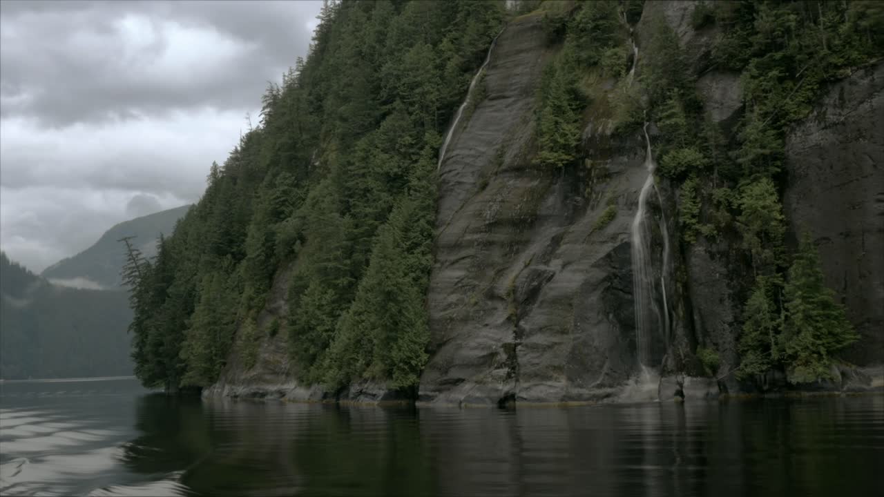 A rocky mountain, in an Alaskan fjord, features several small waterfalls as the camera rotates around the mountain itself