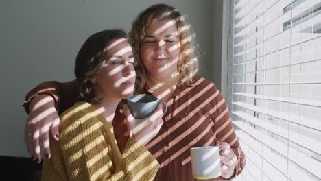 caucasian lesbian couple embracing and drinking coffee