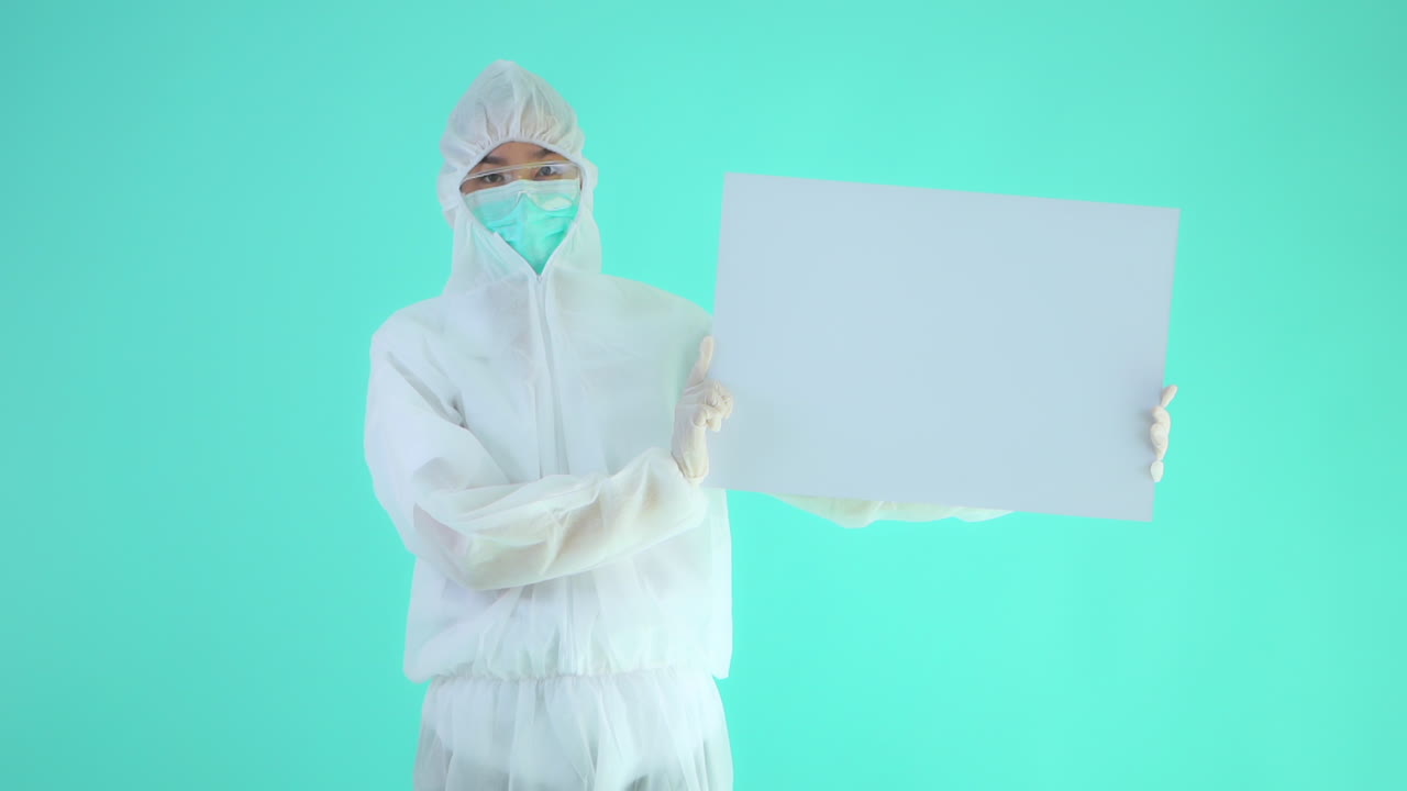 Person in Protective Medical Suit Holding and Showing White Board For Logo of Slogan, Isolated on Turquoise Background