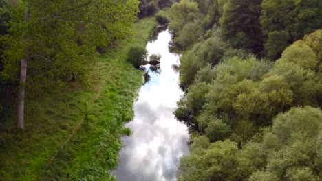 aerial close shot of the calm stream hidden in the woods with clouds reflecting on the water - little ouse river near thetford in the uk