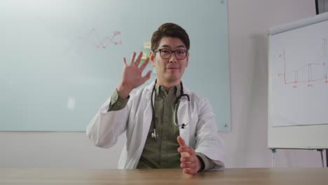 Portrait-of-asian-doctor-smiling-and-waving-on-video-call-looking-at-the-camera