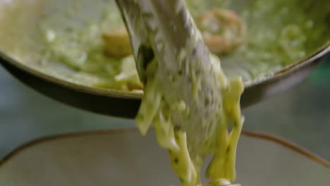 chef places seafood white sauce pasta on plate with tongs