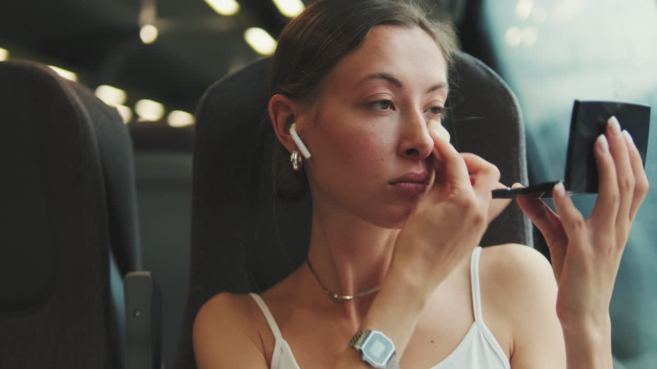 Giovane donna che si trucca mentre viaggia in treno