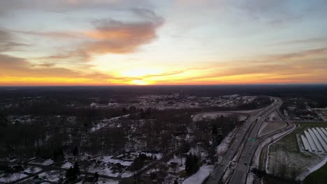 drone footage of a beautiful sunset casting vibrant hues over a snowy landscape and a winding highway, capturing the serene yet dynamic interplay of nature and infrastructure