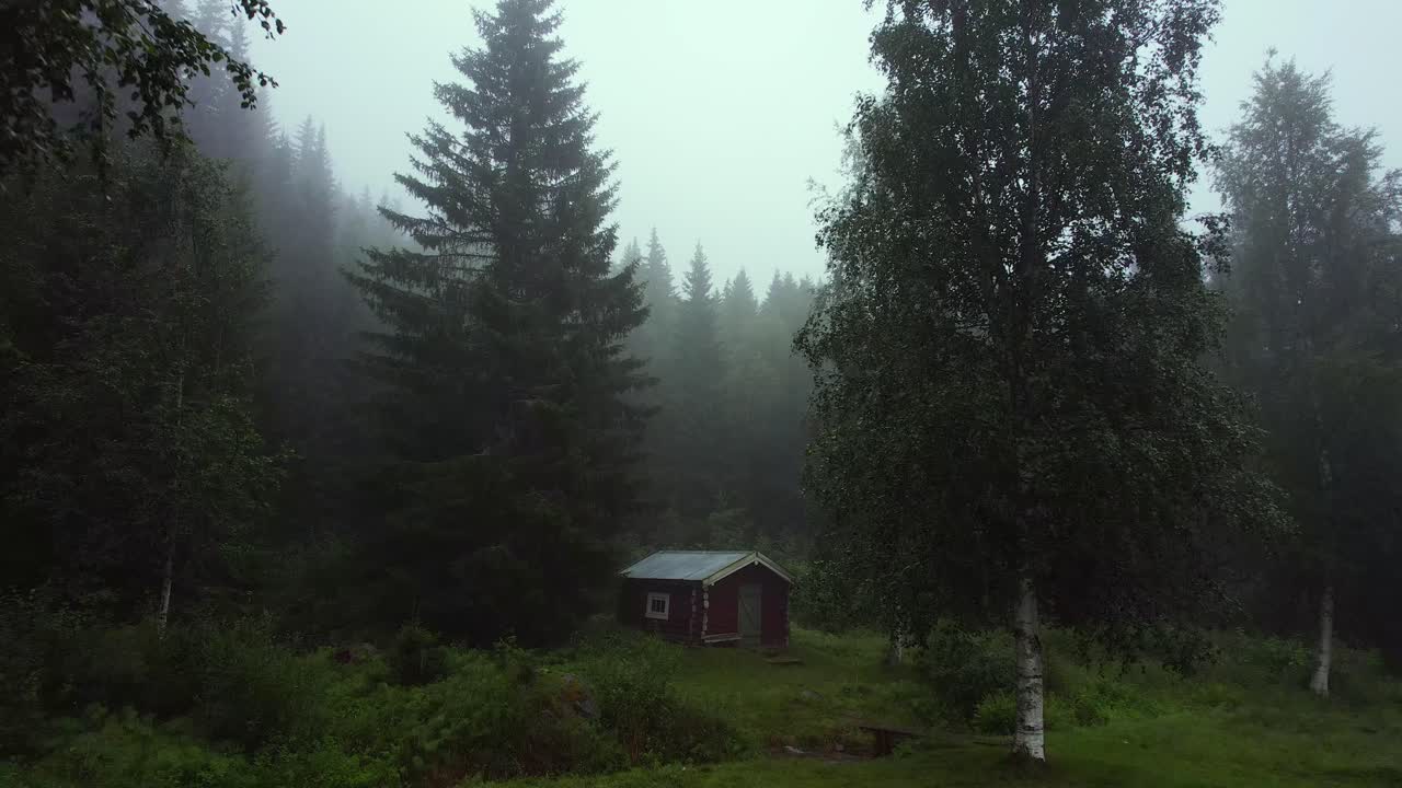 Dolly in bird's eye view of a single cabin with a river and isolated in nature in a misty forest in Unset Norway