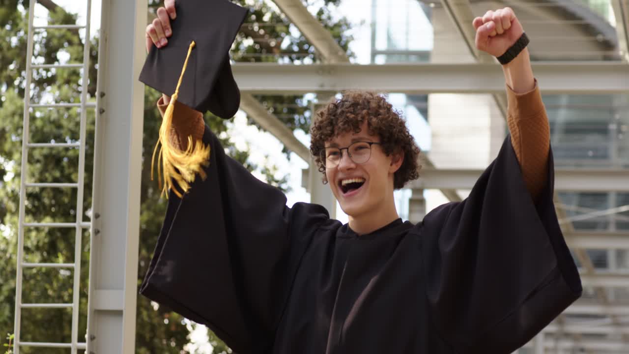 Uomo adulto in toga entra in un passaggio coperto, poi si toglie il tocco, stringe il pugno festeggiando la laurea.
