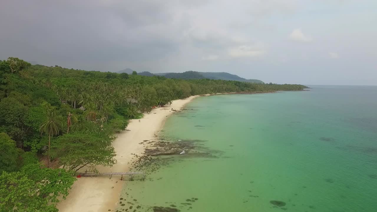 toma aérea de una playa en una isla tropical tailandesa con cocoteros y jungla y resort y océano claro en koh kood, tailandia