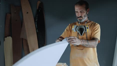 hombre tranquilo dando forma a la tabla de surf con un instrumento