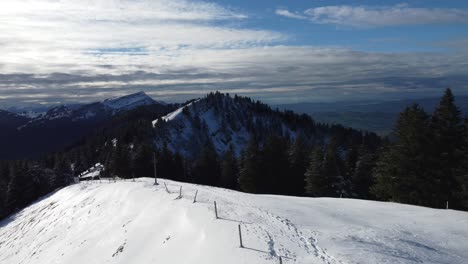 Ich-Folge-Einem-Mann,-Der-Auf-Einem-Schneefeld-Mit-Bergen-Im-Hintergrund-Spazieren-Geht