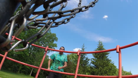 A-unique-perspective-from-inside-the-disc-golf-basket-captures-a-man-celebrating-a-successful-shot,-set-against-a-clear-blue-sky