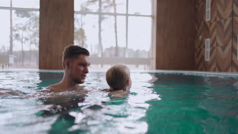 dad is teaching daughter to swim in indoor pool of modern wellness spa family weekend