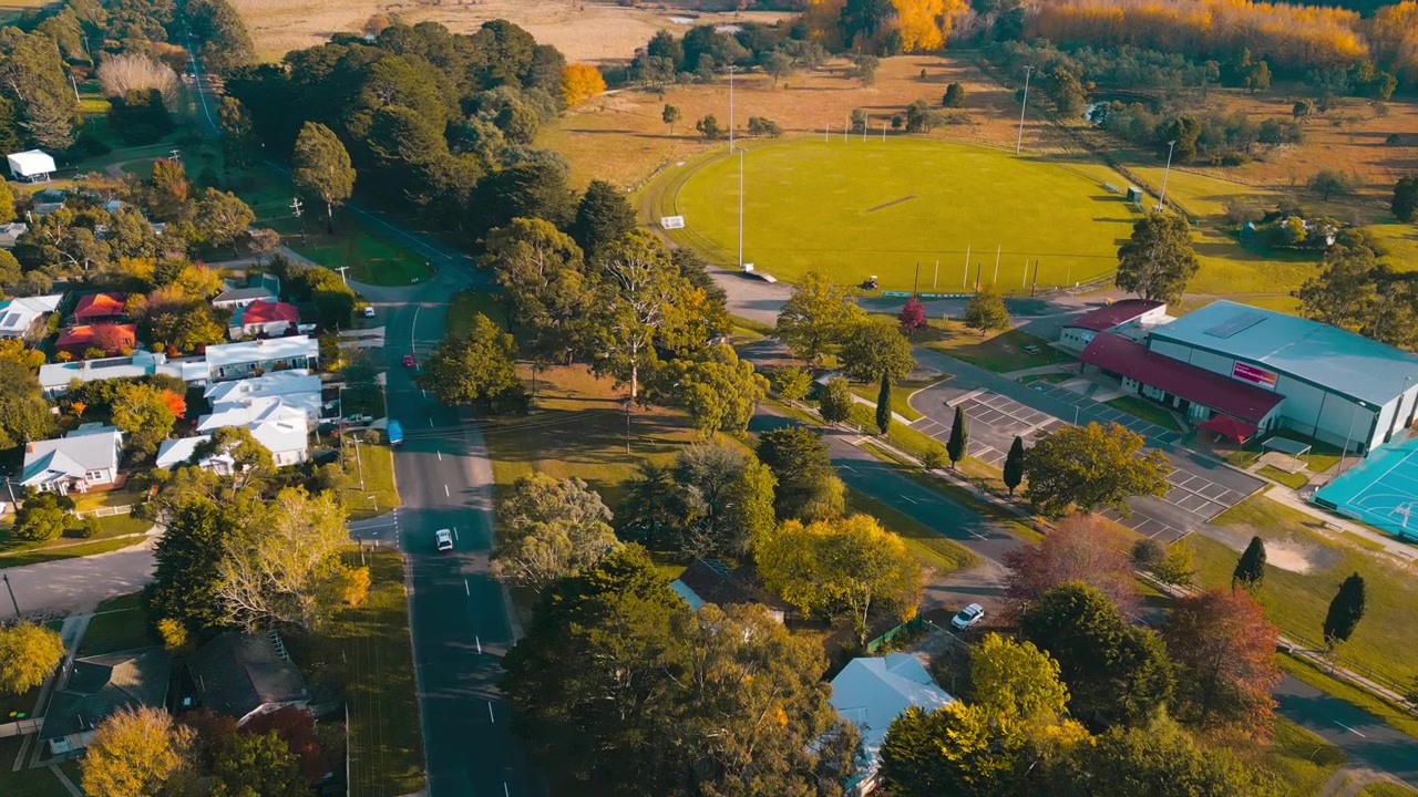 Riprese aeree del paesaggio di case residenziali a Woodend incorniciate da alberi autunnali colorati e dalla calda luce del sole mattutino nella pittoresca regione di Victoria