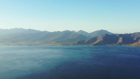 Misty-morning-over-peaceful-tropical-landscape-with-clear-sky,-panoramic-mountains-and-blue-azure-sea-in-Indonesia,-copy-space