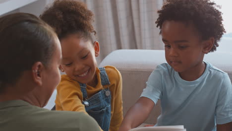 Nahaufnahme-Einer-Mutter-Zu-Hause-Im-Wohnzimmer-Mit-Kindern,-Die-Gemeinsam-Auf-Dem-Sofa-Ein-Buch-Lesen