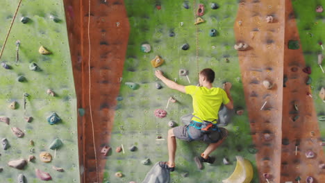 climber moves on the mountain in a room with a rope on the insurance and a bag for chalk overcoming the height rises to the top in slow motion