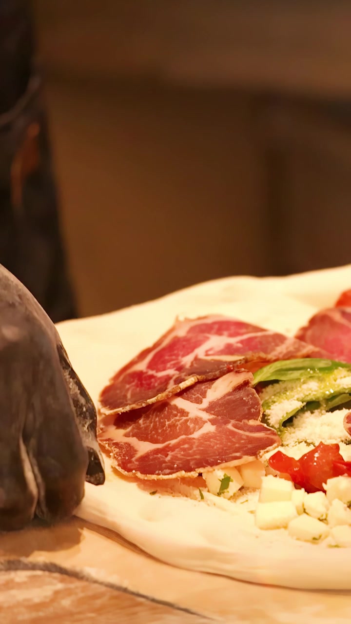 Chef che prepara pizza gourmet con salumi in una cucina professionale.