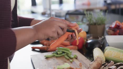 Midsection of african american plus size woman peeling carrot in kitchen, slow motion