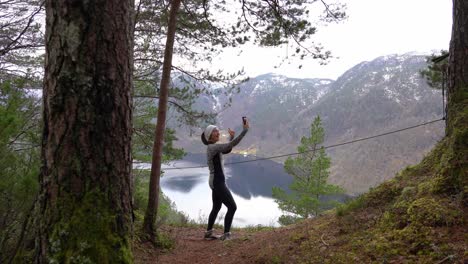 female hiker at scenic overlook uses cell phone and poses to take selfie for social media