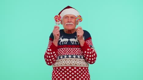 grandfather in christmas sweater holding candy striped lollipops hiding behind them fooling around