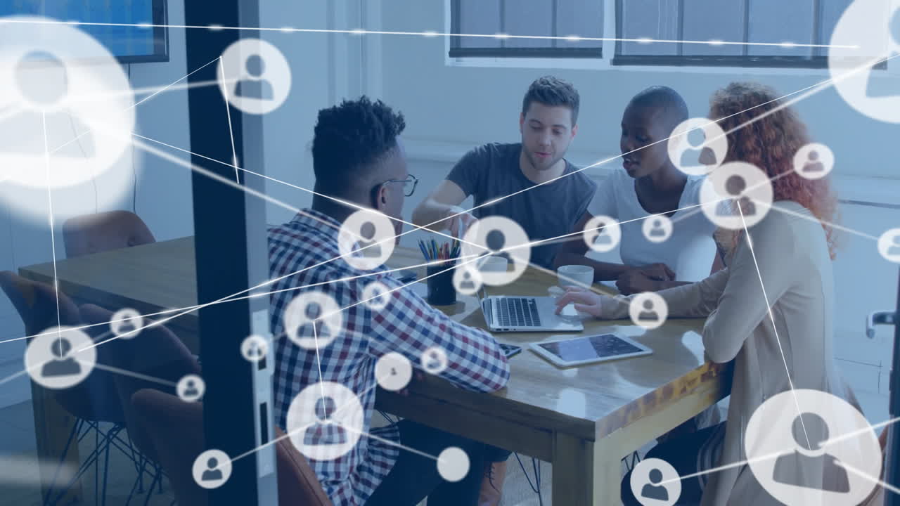 Team collaborating around table, using laptop and tablet with floating business networking icons