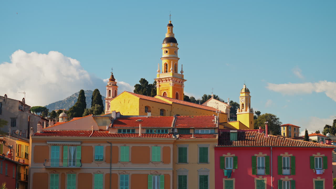 Distant view of the St Michel Basilica surrounded by colourful buildings and palm trees, Menton, France