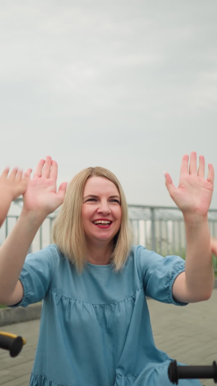 A mother and her two children share a joyful moment trying to give each other high fives, she's squatting with iron rail and greenery by the side